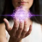 En kvinna håller upp sin hand där ett lysande lila kronchakra svävar.