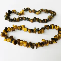 Två armband av tiger eye-stenar, med sina karakteristiska gyllene och bruna ränder, ligger på en vit bakgrund.