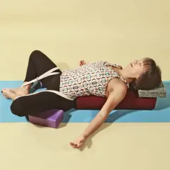 Kvinna i supta baddha konasana med stöd av bolster och block.