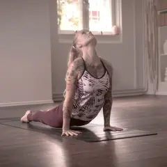 En kvinna med tatueringar utför en uppåtgående hund i dakini yoga.