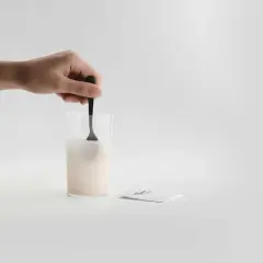 En hand rör om pulver i ett glas med vatten. Bredvid ligger ett paket med sibo probiotika, redo att blandas för en hälsosam start.