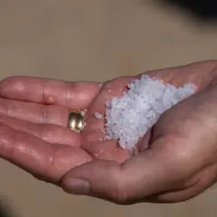 En hand håller en guldring och en hög med kristallsalt.