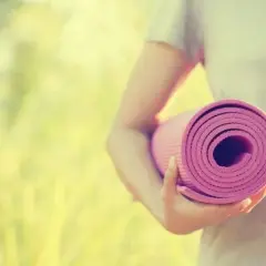 Person håller en rullad rosa yogamatta i solljus. Dags för yoga utomhus.