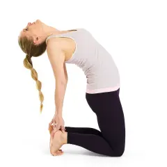 Kvinna i kamelen yoga-ställning, med ryggen böjd bakåt och händerna vid fötterna. Håret är flätat.