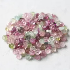 En hög med små, fasetterade turmalinstenar i nyanser av rosa, lila och grönt. Dessa stenar sägs ha helande rosa turmalin egenskaper.