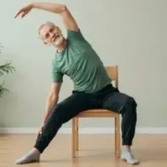 Äldre man gör senior yoga på en stol, sträcker sig åt sidan med ett leende.