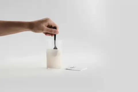 En hand rör om pulver i ett glas med vatten. Bredvid ligger ett paket med sibo probiotika, redo att blandas för en hälsosam start.