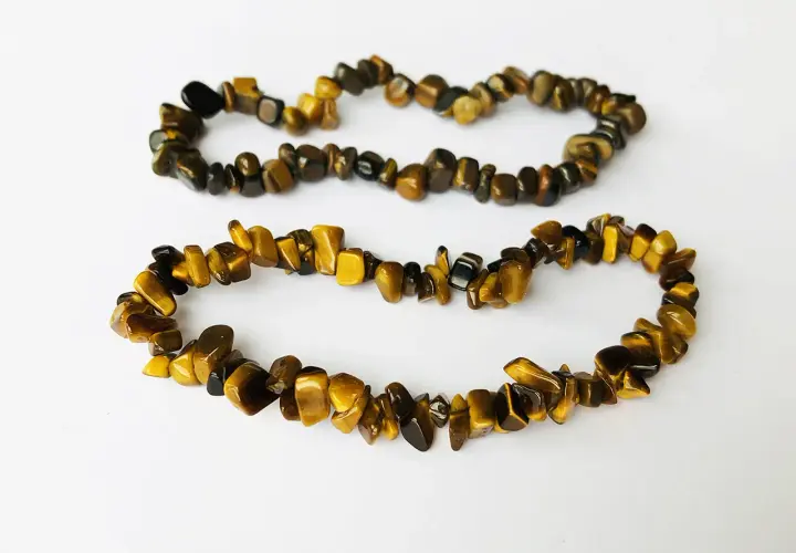 Två armband av tiger eye-stenar, med sina karakteristiska gyllene och bruna ränder, ligger på en vit bakgrund.