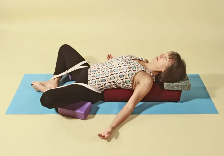 Kvinna i supta baddha konasana med stöd av bolster och block.