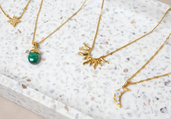 Fyra guldfärgade halsband med olika hängen: en stjärna, en grön sten, en sol och en måne. Vilken kristall passar mig?