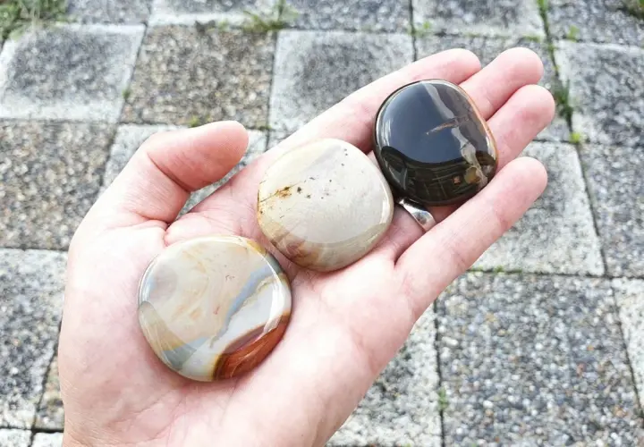 Hand håller tre polerade stenar. En mörk, en ljus med bruna strimmor, och en med blå och bruna mönster. Dessa polykrom jaspis egenskaper är fascinerande.