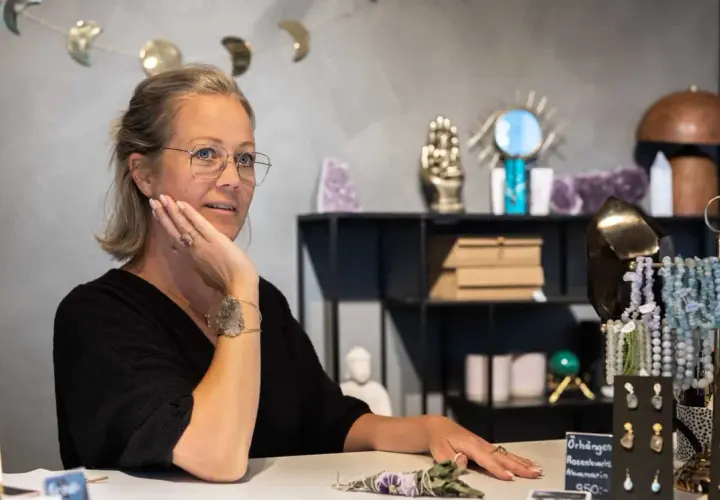 Kvinna med glasögon i butik med kristaller. Hon pratar om apatit betydelse, kanske om dess helande krafter.