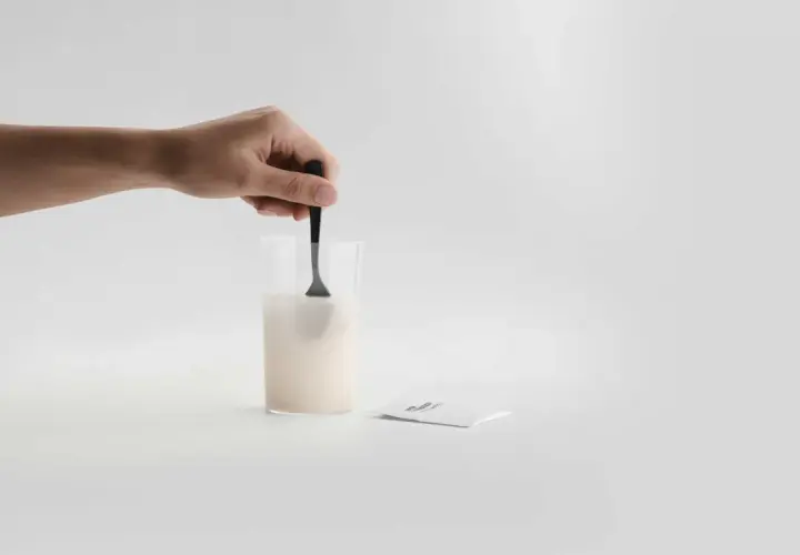 En hand rör om pulver i ett glas med vatten. Bredvid ligger ett paket med sibo probiotika, redo att blandas för en hälsosam start.