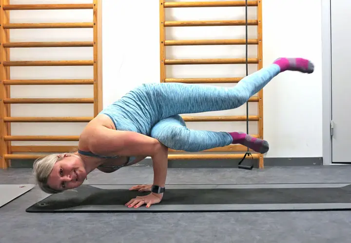 En kvinna utför en kråkan yoga-position på en yogamatta, med benen utsträckta och kroppen balanserad på händerna.