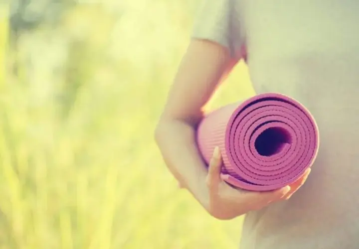 Person håller en rullad rosa yogamatta i solljus. Dags för yoga utomhus.