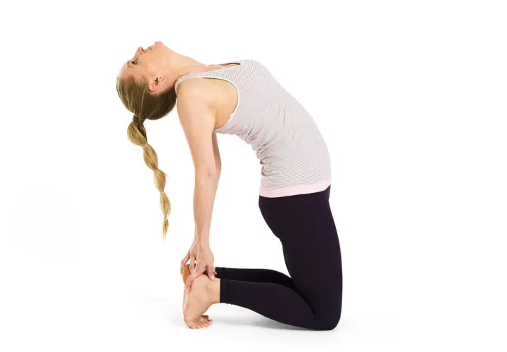 Kvinna i kamelen yoga-ställning, med ryggen böjd bakåt och händerna vid fötterna. Håret är flätat.