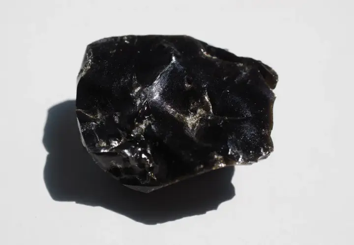 En bit glänsande, svart obsidian svenska, med en skugga som faller åt vänster.