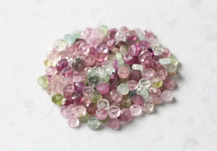 En hög med små, fasetterade turmalinstenar i nyanser av rosa, lila och grönt. Dessa stenar sägs ha helande rosa turmalin egenskaper.
