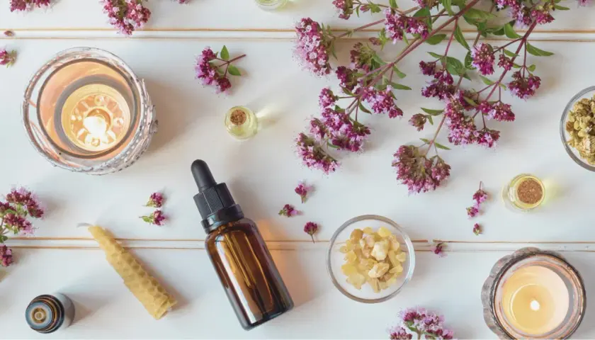 En lugnande scen med aromaterapi oljor, tända ljus, örter och blommor.