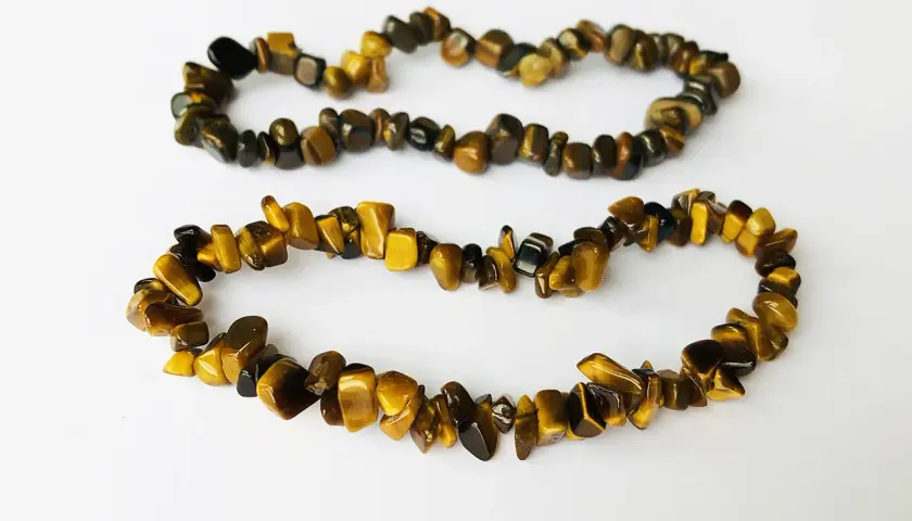 Två armband av tiger eye-stenar, med sina karakteristiska gyllene och bruna ränder, ligger på en vit bakgrund.
