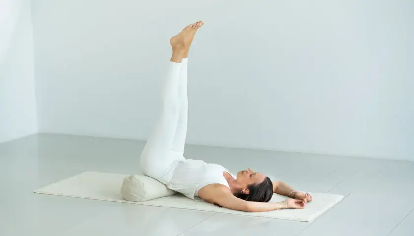 Kvinna i vit klädsel utför yoga, benen uppåt. En lugnande position som kan hjälpa vid yoga klimakteriet.