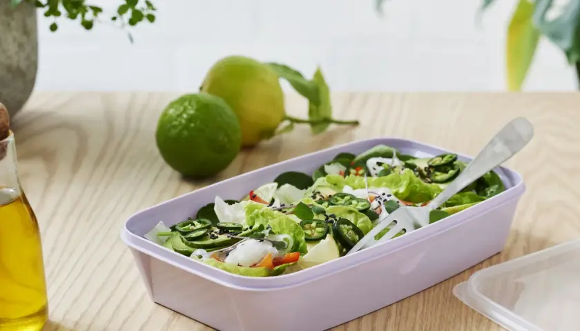 En fräsch sallad med gröna blad, jalapeños och avokado i en lila matlåda. Perfekt för **organisk mat** på språng.