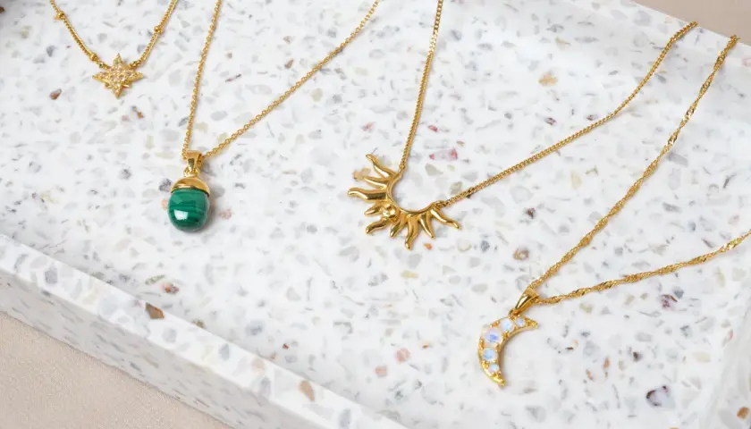 Fyra guldfärgade halsband med olika hängen: en stjärna, en grön sten, en sol och en måne. Vilken kristall passar mig?