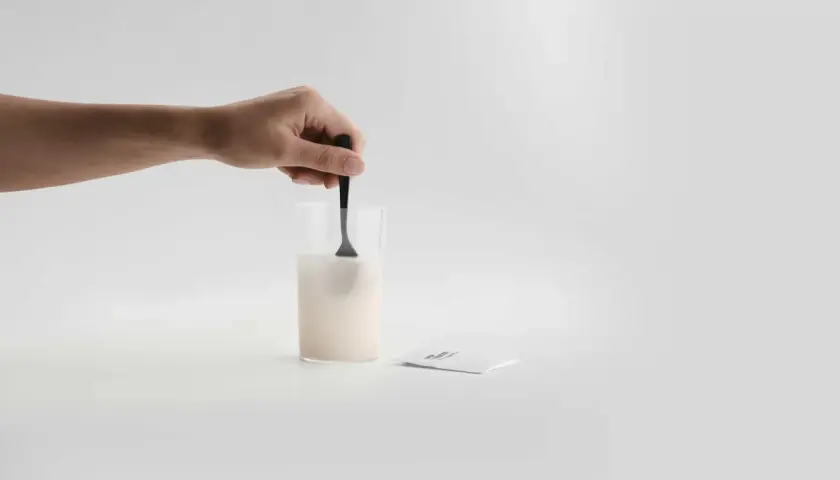 En hand rör om pulver i ett glas med vatten. Bredvid ligger ett paket med sibo probiotika, redo att blandas för en hälsosam start.