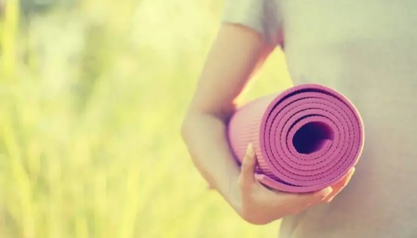 Person håller en rullad rosa yogamatta i solljus. Dags för yoga utomhus.