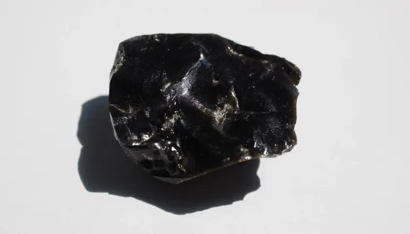 En bit glänsande, svart obsidian svenska, med en skugga som faller åt vänster.