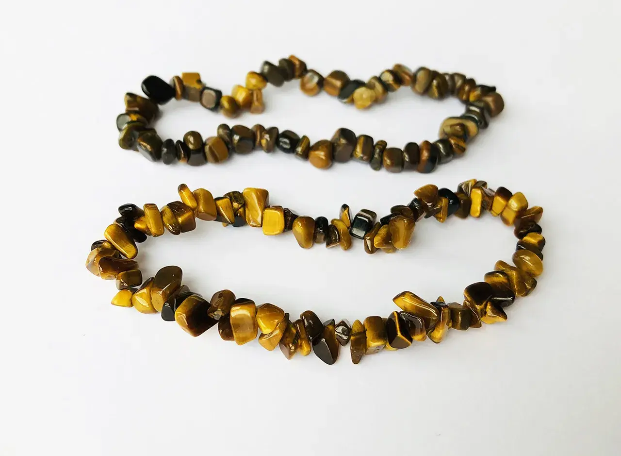Två armband av tiger eye-stenar, med sina karakteristiska gyllene och bruna ränder, ligger på en vit bakgrund.