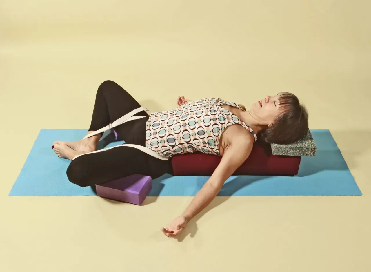 Kvinna i supta baddha konasana med stöd av bolster och block.