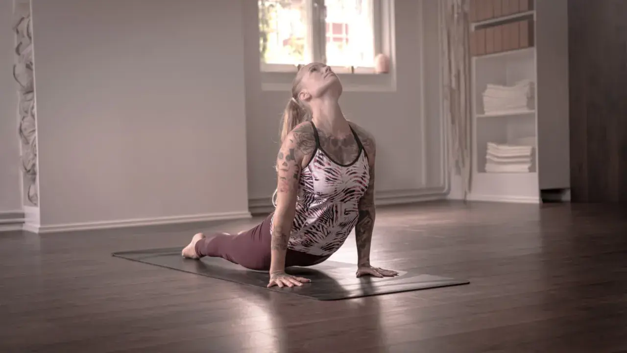 En kvinna med tatueringar utför en uppåtgående hund i dakini yoga.
