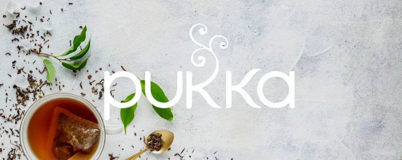 En kopp te med en tepåse, teblad och sockerbitar. Texten "PUKKA" i vitt. En sann pukka love för teälskare.