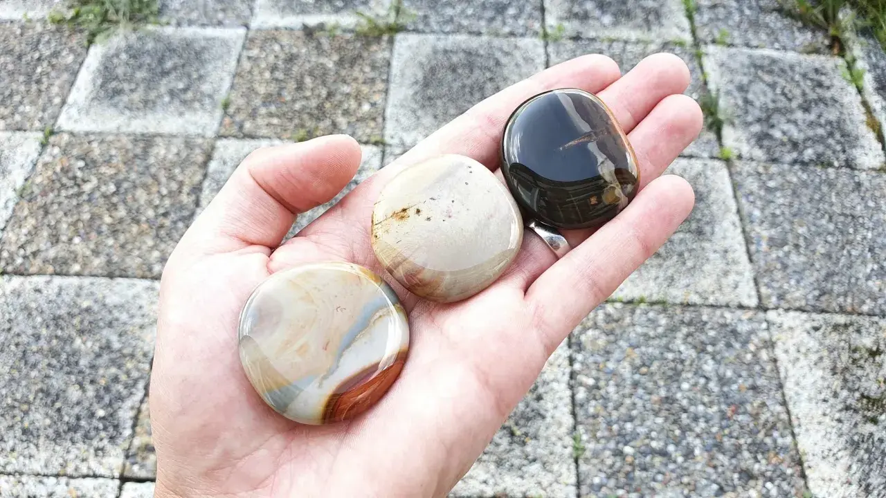 Hand håller tre polerade stenar. En mörk, en ljus med bruna strimmor, och en med blå och bruna mönster. Dessa polykrom jaspis egenskaper är fascinerande.