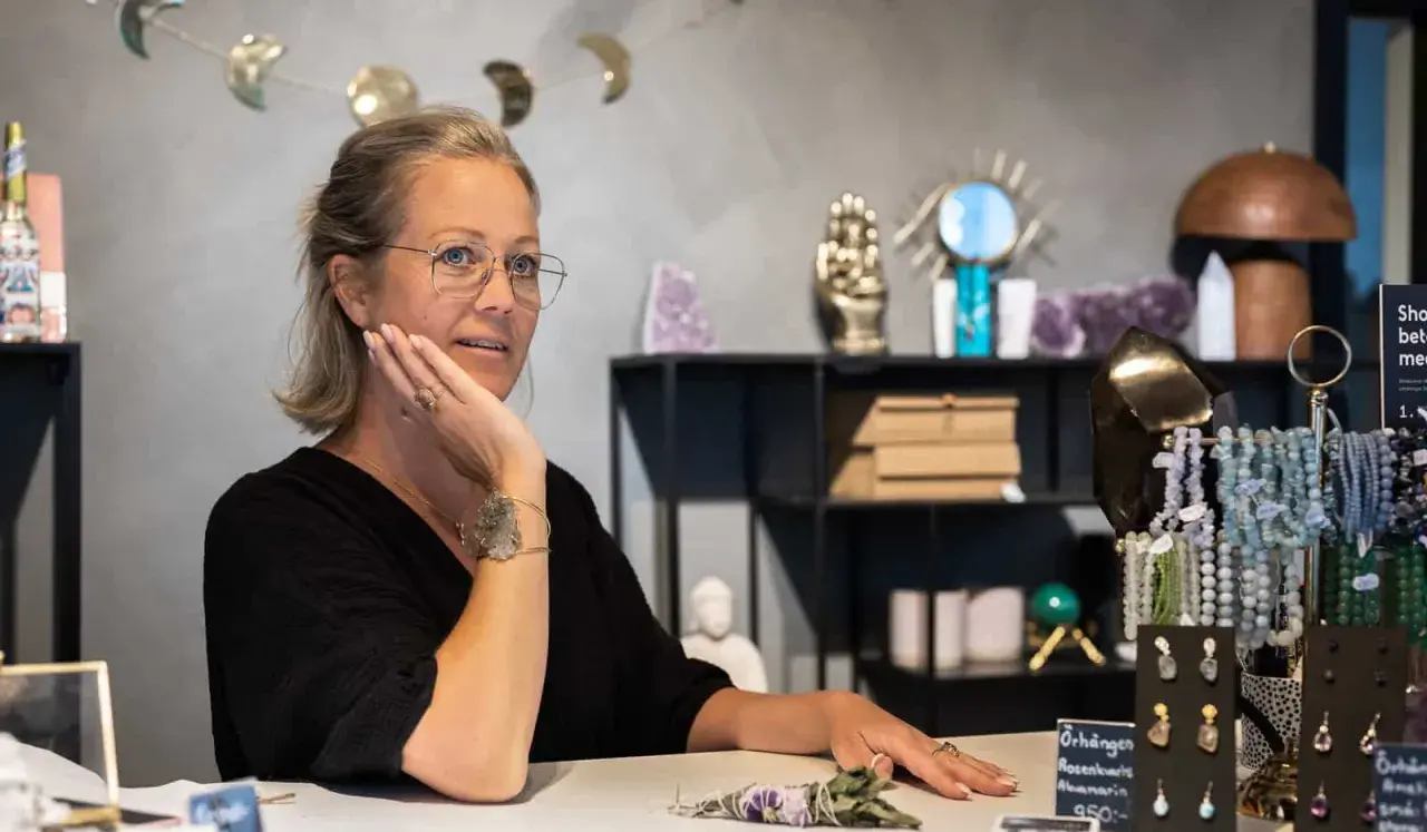 Kvinna med glasögon i butik med kristaller. Hon pratar om apatit betydelse, kanske om dess helande krafter.