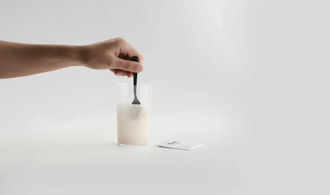 En hand rör om pulver i ett glas med vatten. Bredvid ligger ett paket med sibo probiotika, redo att blandas för en hälsosam start.