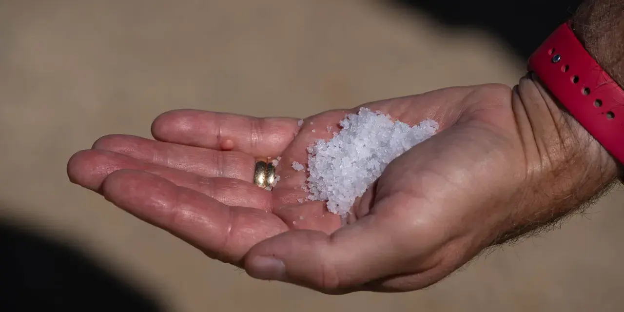En hand håller en guldring och en hög med kristallsalt.