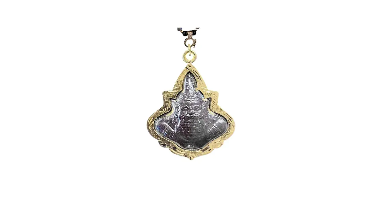 Ett detaljerat buddha halsband med en ansiktsliknande amulett i en guldfärgad ram.
