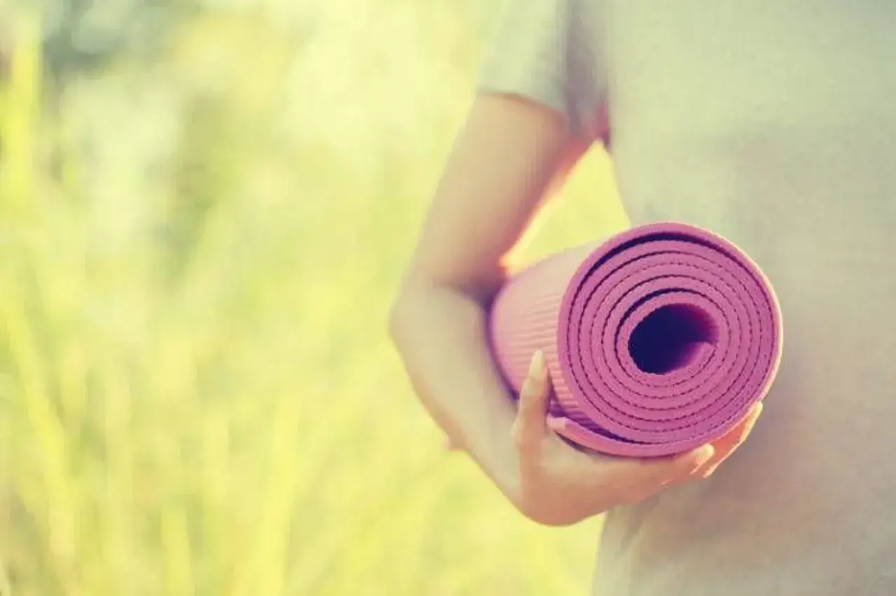 Person håller en rullad rosa yogamatta i solljus. Dags för yoga utomhus.