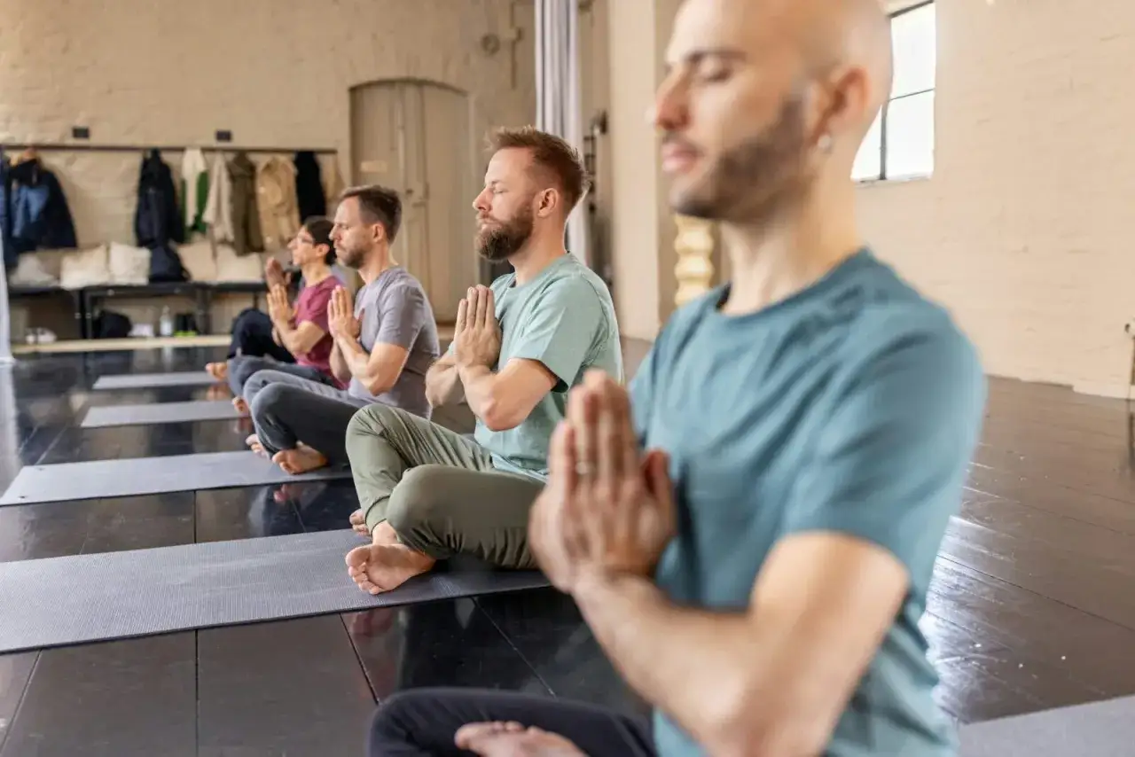 M&auml;n sitter p&aring; yogamattor i meditation, med h&auml;nderna i b&ouml;nest&auml;llning. Namaste betyder 
