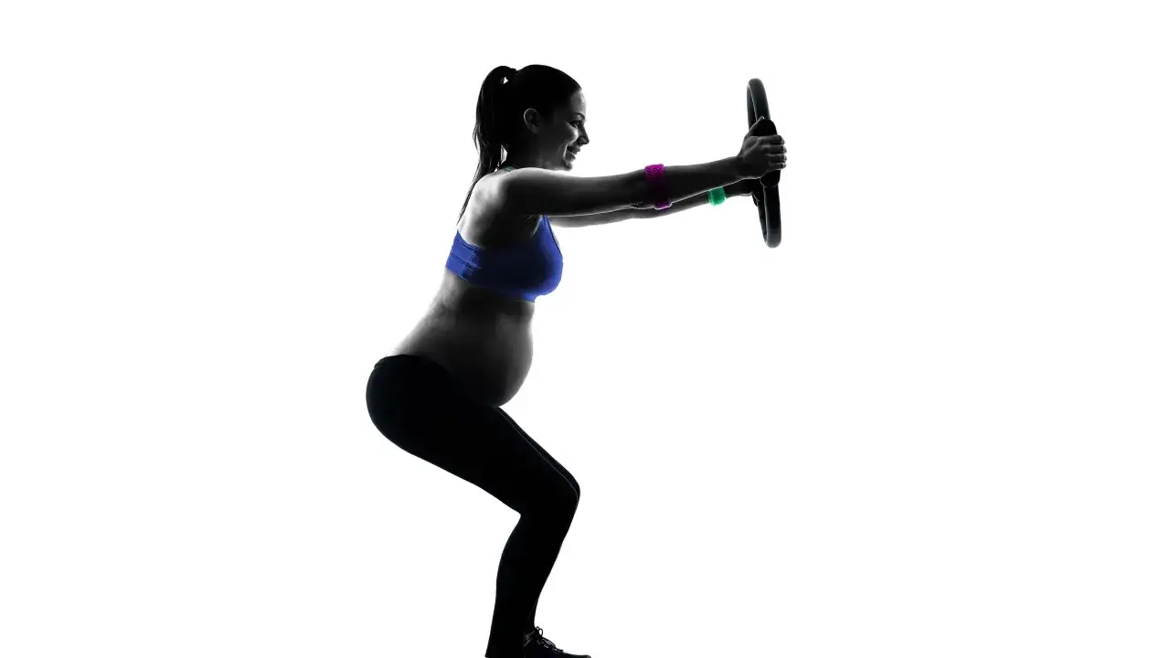 Gravid kvinna tr&auml;nar pilates med en ring. Hon g&ouml;r en kn&auml;b&ouml;j och h&aring;ller ringen framf&ouml;r sig.