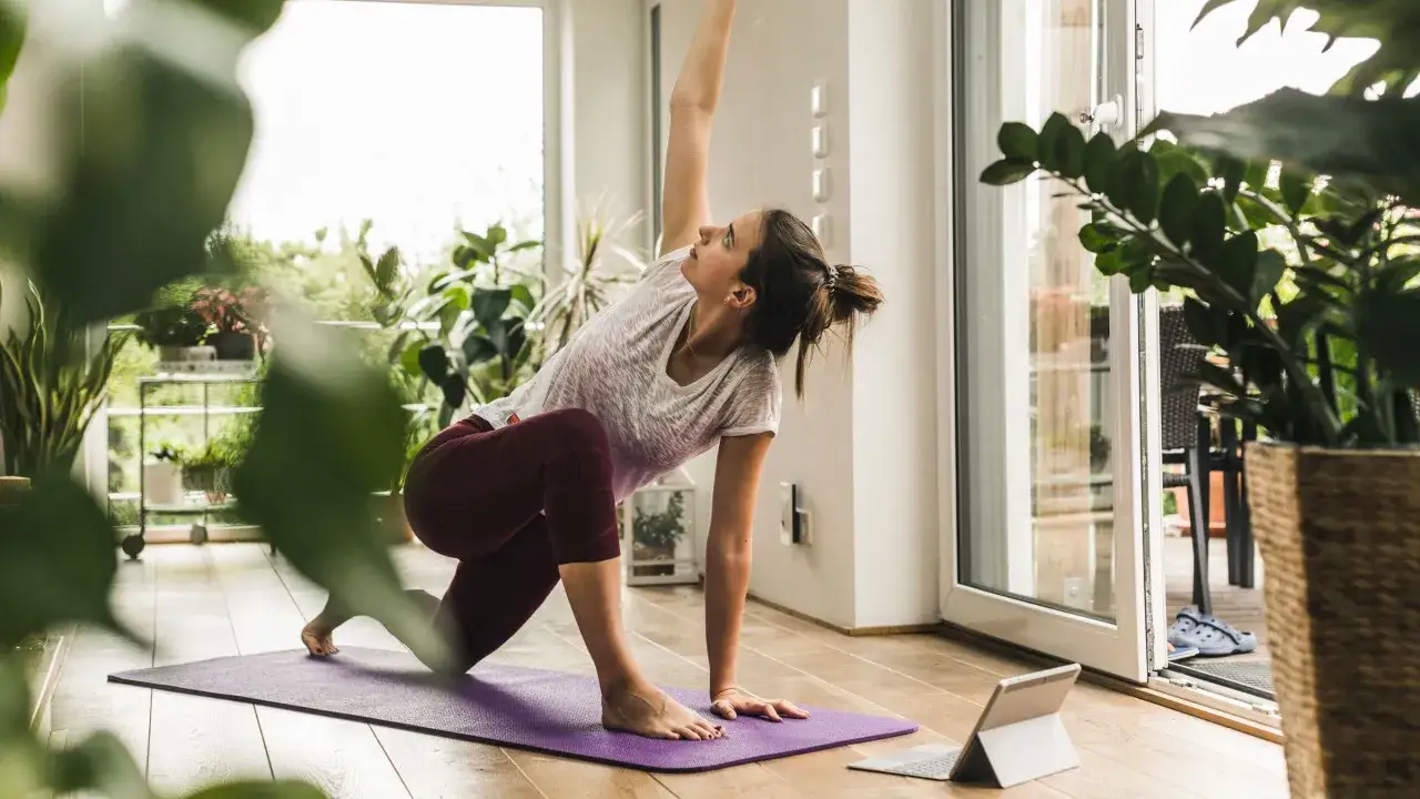 Kvinna utför yogaposition framför en surfplatta, som om hon följer en yoga dvd.