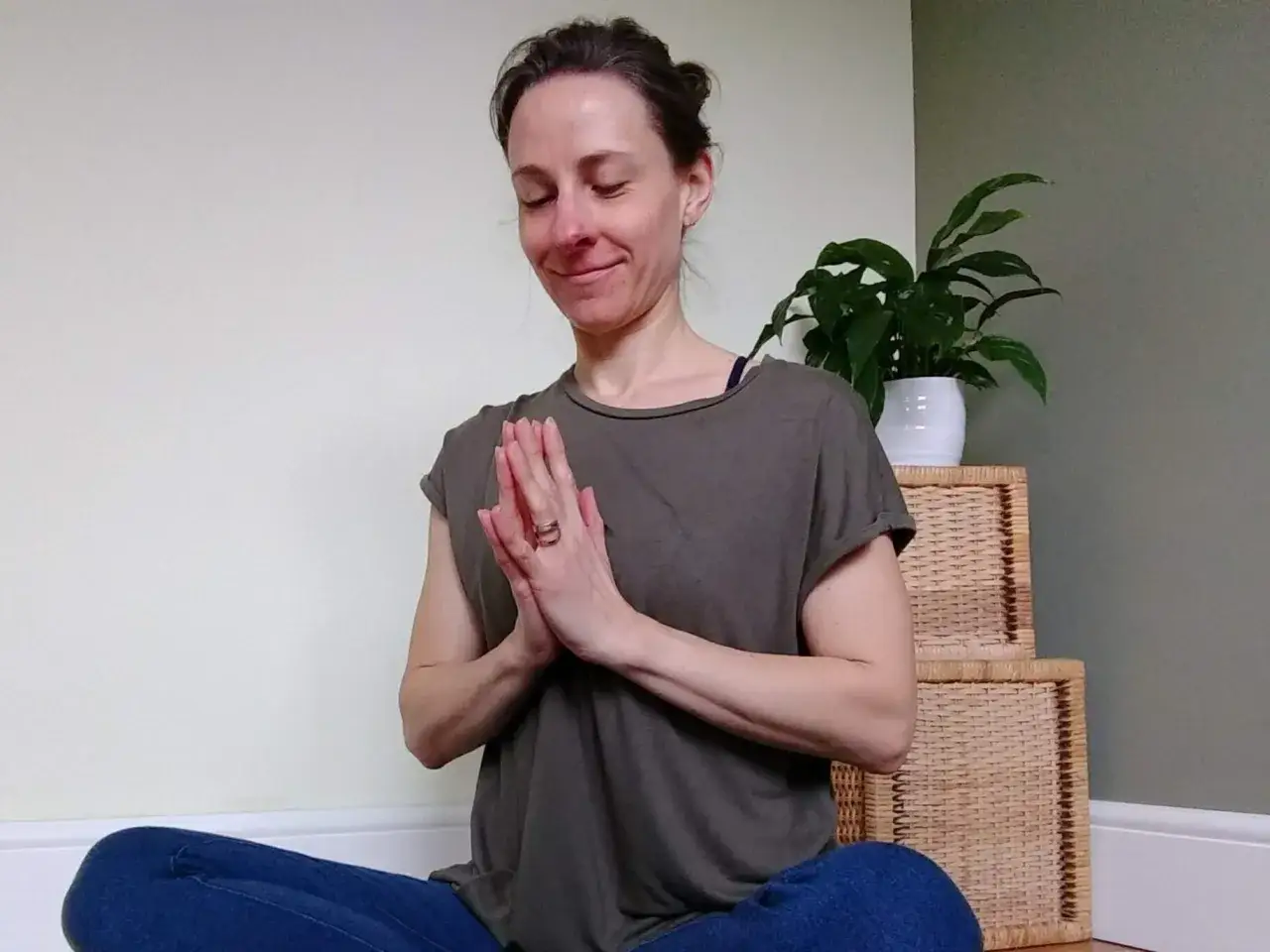 Kvinna i meditationsst&auml;llning med slutna &ouml;gon och h&auml;nderna i namaste. Hon utstr&aring;lar lugn och frid, ett sant namaste spr&aring;k.