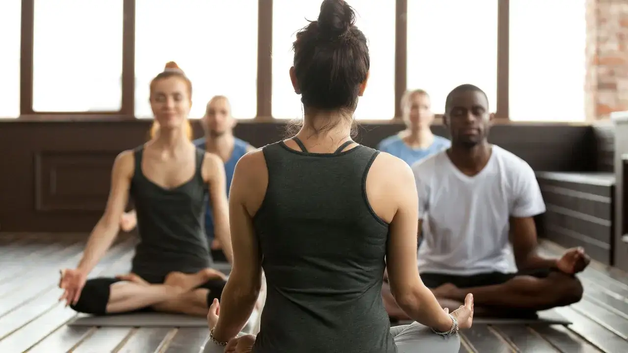 En grupp m&auml;nniskor sitter i lotusst&auml;llning under en yogaklass. De ut&ouml;var yoga, en andlig praktik som kan liknas vid en religion f&ouml;r vissa.