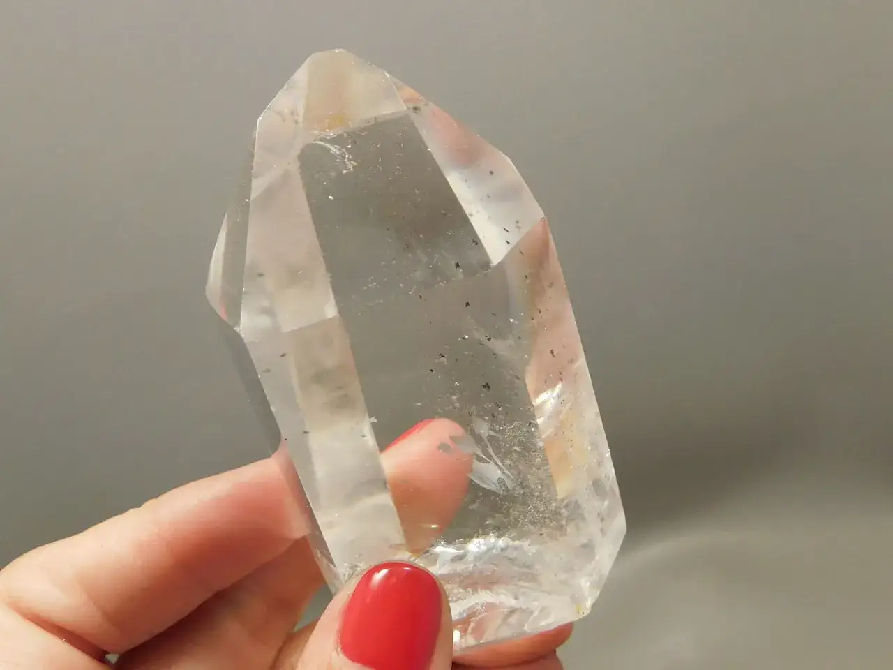 En hand med r&ouml;tt nagellack h&aring;ller en stor, klar bergkristall. Denna bergkristall, &auml;ven k&auml;nd som 