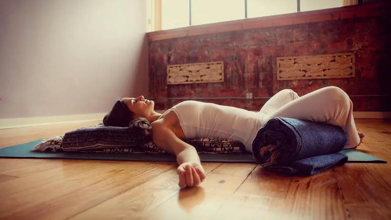 Kvinna i avslappnad position med en rullad filt som en restorative yoga positioner under kn&auml;na.