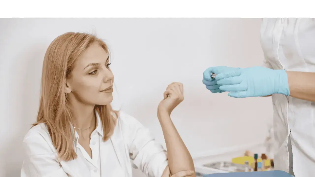 Kvinna f&ouml;rbereder sig f&ouml;r ett b12 test. En sjuksk&ouml;terska i bl&aring; handskar h&aring;ller en provr&ouml;r.