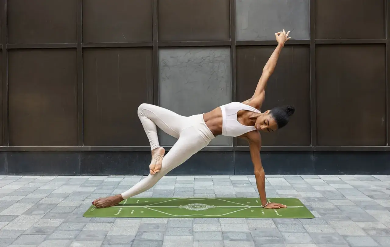 En kvinna utf&ouml;r en utmanande power yoga-position p&aring; en gr&ouml;n matta utomhus.