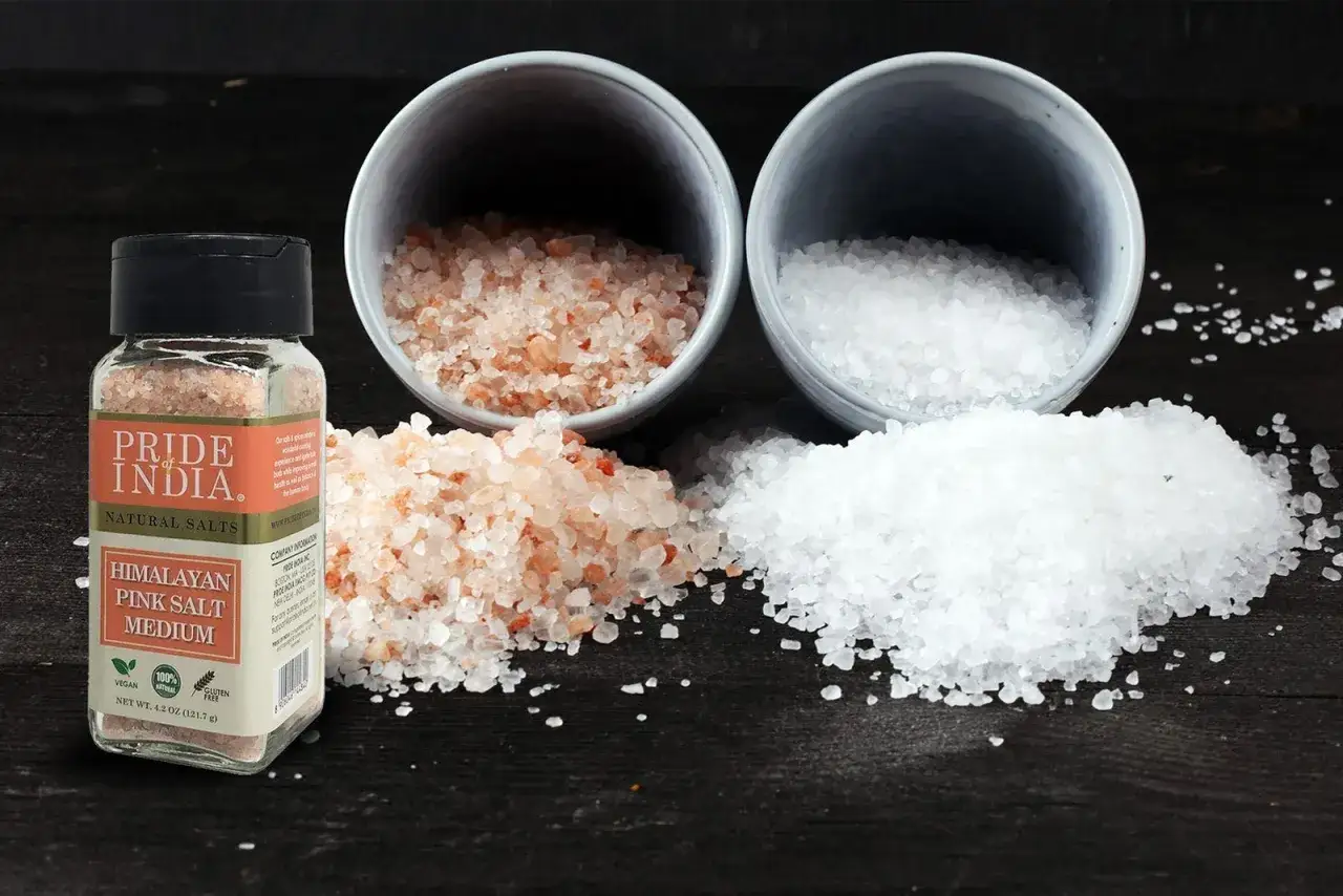 En burk med rosa Himalayasalt och två skålar med salt, en rosa och en vit. Många tror att himalayasalt nyttigt.